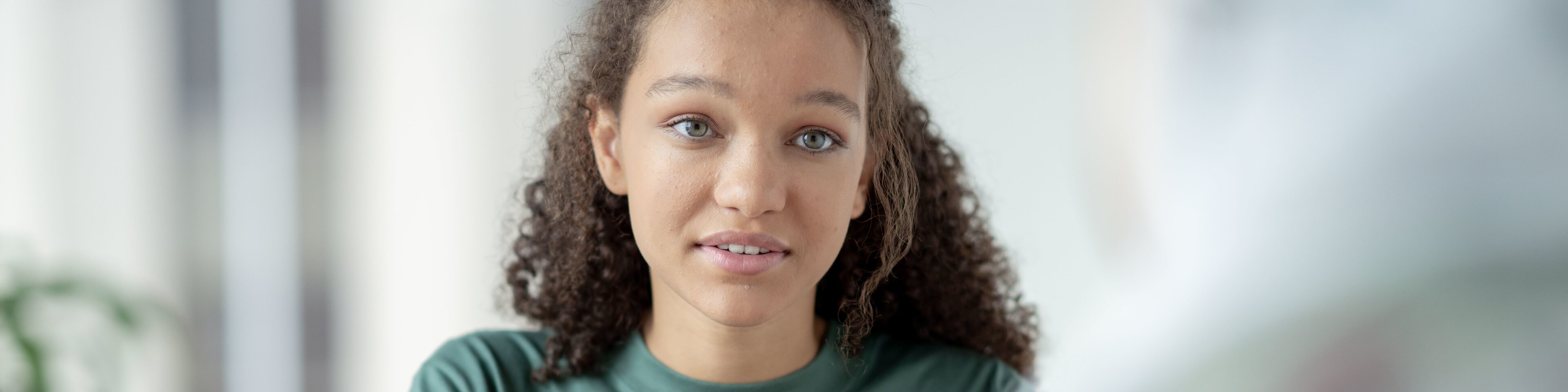 Jugendliches Mädchen mit braunen lockigen Haaren und grünen Augen sitzt an einem Tisch und führt ein Gespräch mit einer Person | © FatCamera - Getty Images